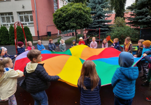 Dzieci bawią się chustą animacyjną w ogrodzie.