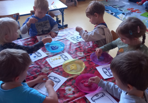 Praca plastyczna. Dzieci robią stemple farbą na kartonowym szablonie słoika.