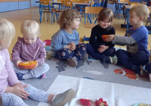 Dzieci siedzą na dywanie i oglądają przekrojoną dynię.