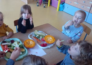 Dzieci siedzą przy stole i jedzą surowe warzywa.
