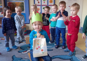 Urodziny. Dzieci stoją w kole, w środku siedzi chłopiec w zielonej koronie na głowie.