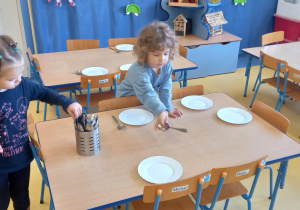 Dzieci nakrywają do stołu - układają łyżki obok talerzy.