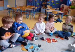 Dzieci siedzą na dywanie i przytulają pluszaka w kształcie kropelki wody.