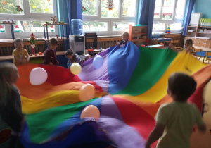 Dzieci bawią się tęczową chustą oraz balonami.