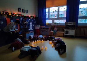 Wigilia grupowa. Dzieci leżą skulone na podłodze wokół zapalonych latarenek.