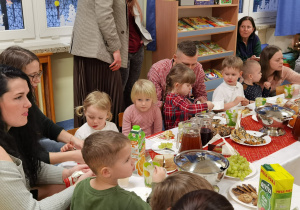 Wigilia grupowa. Dzieci i rodzice siedzą przy wigilijnym stole w sali przedszkolnej.