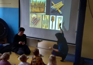 Dzieci oglądają narzędzia rzeźbiarskie na dużym slajdzie.