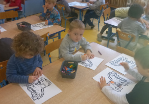 Dzieci siedzą przy stolikach i kolorują sylwetkę konia.