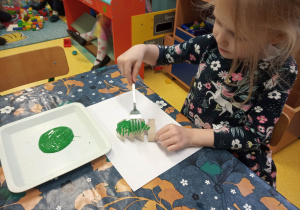 Dziewczynka maluje widelcem choinkę z rolki po papierze.