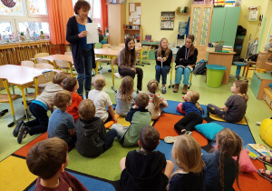 Dzieci słuchają bajek czytanych przez starsze koleżanki ze szkoły.