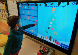 Chłopiec dekoruje choinkę na tablicy interaktywnej.