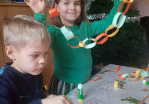 Dzieci tworzą z papieru wspólny łańcuch na choinkę.