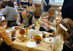 Dzień Babci i Dziadka w przedszkolu. dzieci i ich bliscy siedzą przy stolikach.