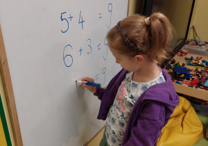Dziewczynka zapisuje na tablicy działania matematyczne.