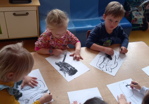 dzieci rysują węglem na kartkach.