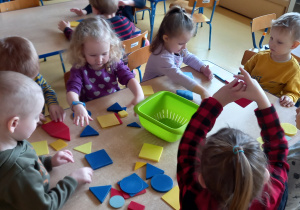 Dzieci siedzą przy stolikach i układają budowle figur geometrycznych.