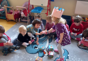 Urodziny. Dziewczynka w koronie rozdaje dzieciom małe pudełka z puzzlami.