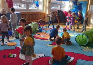 Dzieci bawią się swobodnie sprzętem sportowym w sali gimnastycznej.