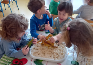 Dzieci odciskają ślady zabawkowych dinozaurów w masie solnej.