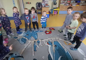 Dzieci stoją wokół szkieletu dinozaura z rolek od papieru tolaletowego.