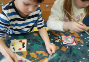 Chłopiec i dziewczynka malują farbami drewniane kafelki.