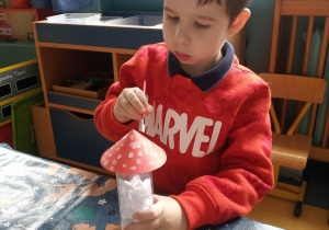 Chłopiec maluje pędzlem kapelusz muchomora.
