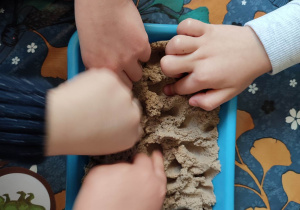 Dzieci szukają ukrytych kości dinozaurów w piasku kinetycznym.