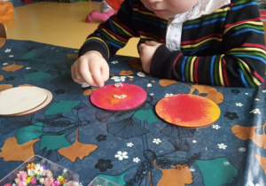 Chłopiec ozdabia kwiatkami pomalowany drewniany krążek.