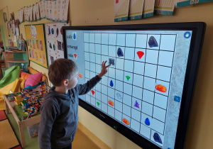 Chłopiec rozwiązuje zadanie z kodowania na tablicy interaktywnej.