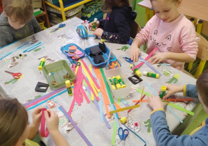 Dzieci sklejają klauny z kolorowych pasków.