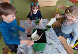 Dzieci sadzą rośliny w doniczkach.