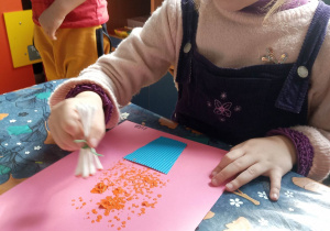 Dziewczynka maluje patyczkami i farbą kwiatki.