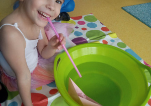 Dziewczynka wykonuje eksperyment z wodą i łódką papierową.