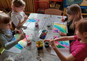 Dzieci malują tło akwarelami do pracy plastycznej o łące.