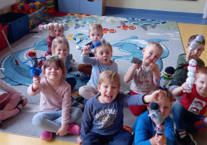 Dzieci siedzą na dywanie i pokazują pacynki zrobione ze skarpetek.
