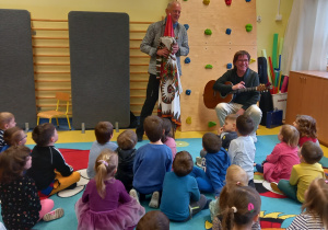 Koncert. Dzieci oglądają ludowy instrument w kształcie skrzata.