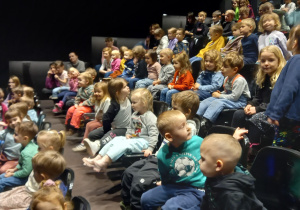 Dzieci siedzą na widowni i oglądają spektakl teatralny.