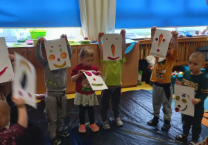Warsztaty malarskie Fundacji Szkatułka. Dzieci pokazują stworzone przez siebie portrety z warzyw i owoców.