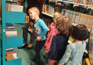 Wizyta w bibliotece szkolnej. Dzieci oglądają księgozbiór zebrany na półkach.