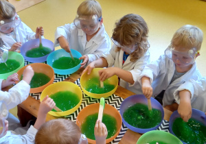 Dzieci mieszają w miseczkach zielona substancję.