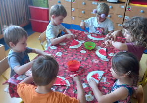 Dzieci malują czerwona farbą papierowy talerzyk.