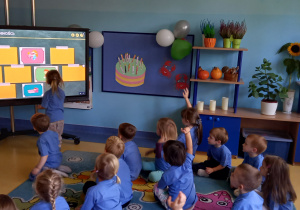 Dzień przedszkolaka. Dzieci odkrywają obrazki na tablicy multimedialnej.