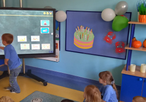 Dzień przedszkolaka. Dzieci układają przedszkolny plan dnia na tablicy multimedialnej.