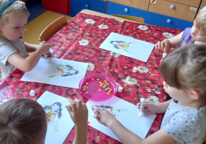 Dzieci przyklejają małe kolorowe listki na sylwetce pani Jesieni.