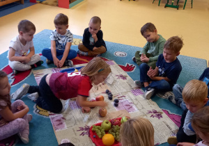 Dzieci siedzą na dywanie i układają owoce.
