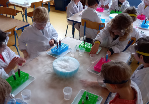 Zajęcia badawcze. Dzieci siedzą przy stole i obserwują parę powstałą z suchego lodu.