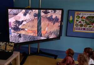 Dzieci oglądają rysunkowy film przyrodniczy na dużym ekaranie.