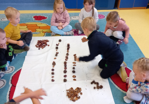 Dzieci układają na dywanie rytmy z kasztanów, szyszek i żołędzi.
