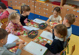 Dzieci siedzą przy stole i kolorują liście w książce dla przedszkolaków.