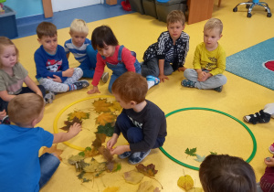 Dzieci siedzą na podłodze i wkładają w obręcze kolorowe jesienne liście.